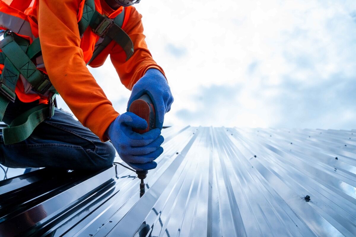 A specialized contractor screws down a metal roof panel.